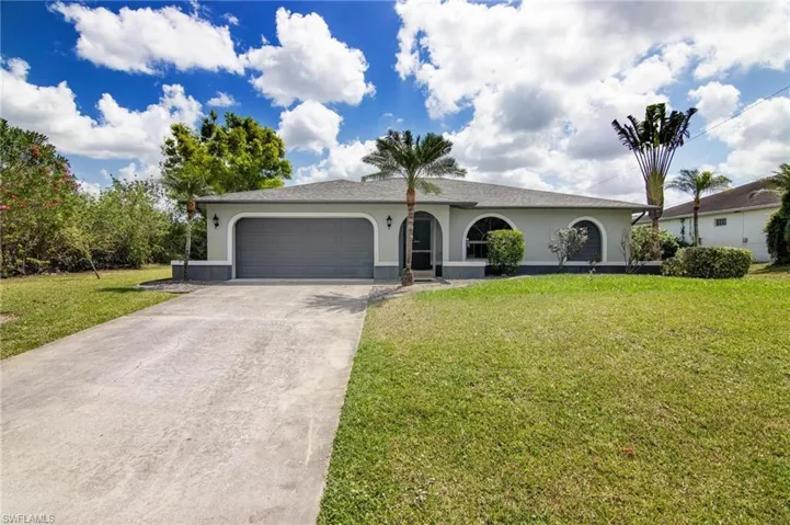 Ranch-style house with concrete driveway, stucco siding, an attached garage, and a front lawn