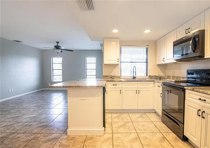 Kitchen with visible vents, a sink, black electric range oven, a peninsula, and white cabinetry
