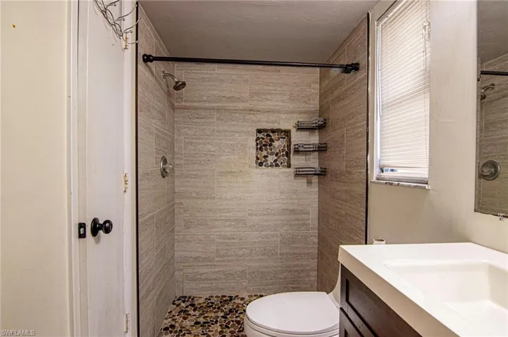 Bathroom featuring a tile shower, vanity, and toilet