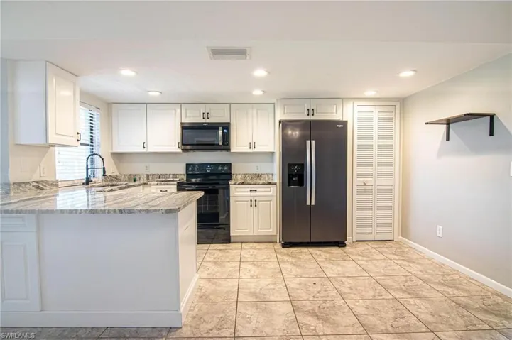 Kitchen with light stone counters, a peninsula, white cabinetry, stainless steel appliances, and a sink