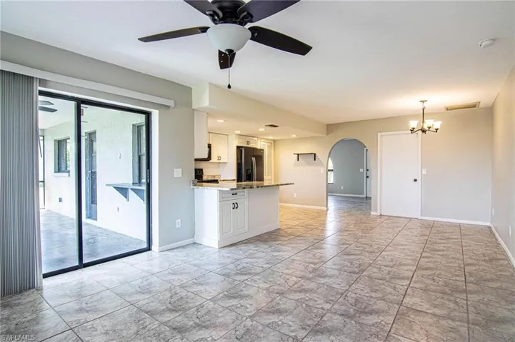 Unfurnished living room with arched walkways, ceiling fan with notable chandelier, and baseboards
