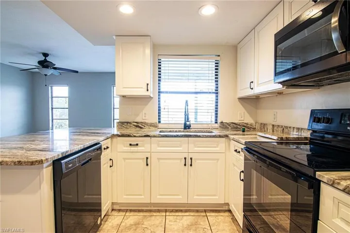 Kitchen featuring ceiling fan, a peninsula, white cabinets, black appliances, and a sink