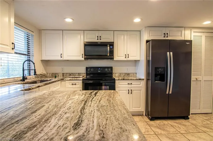Kitchen with white cabinets, light stone countertops, a sink, and appliances with stainless steel finishes