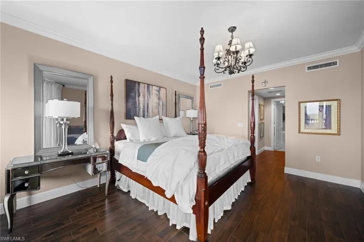 Bedroom with dark wood-type flooring, a notable chandelier, and crown molding