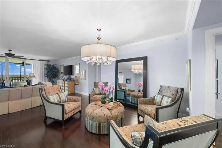 Living room with ceiling fan with notable chandelier, dark hardwood / wood-style flooring, and ornamental molding