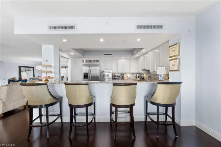 Kitchen with a kitchen bar, stainless steel appliances, kitchen peninsula, dark wood-type flooring, and white cabinets