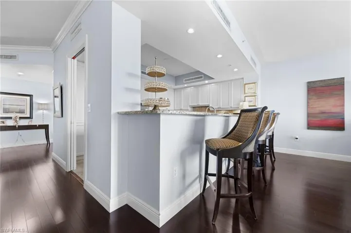 Kitchen with dark wood-type flooring, light stone counters, kitchen peninsula, and white cabinets