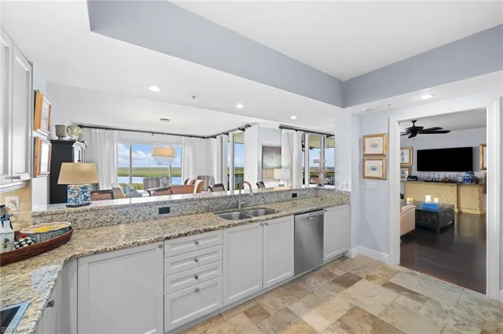 Kitchen featuring white cabinets, light stone countertops, sink, ceiling fan, and stainless steel dishwasher