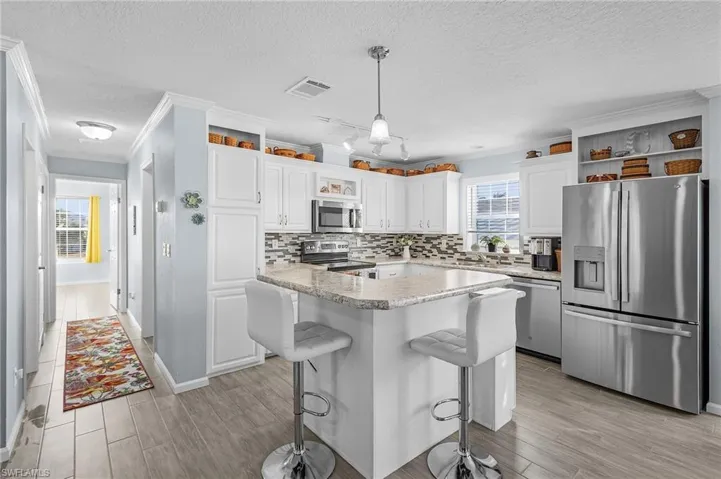 Kitchen with white cabinetry, a kitchen breakfast bar, stainless steel appliances, and hanging light fixtures