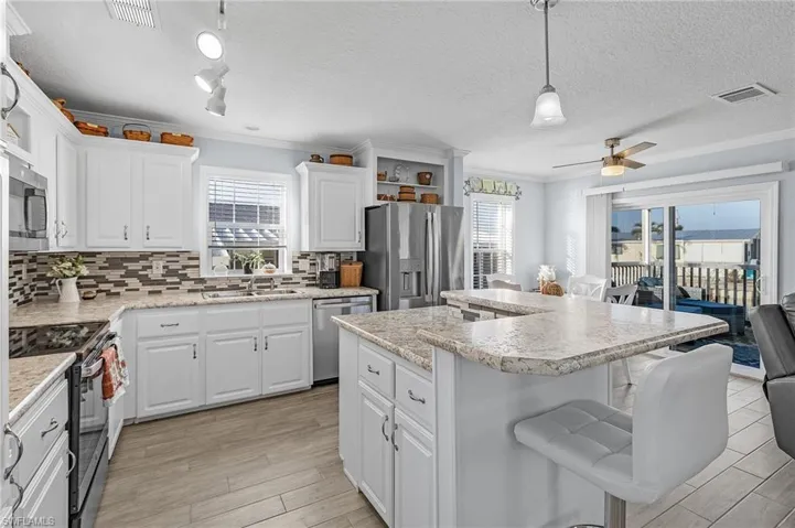 Kitchen with stainless steel appliances, a center island, ceiling fan, white cabinetry, and decorative light fixtures