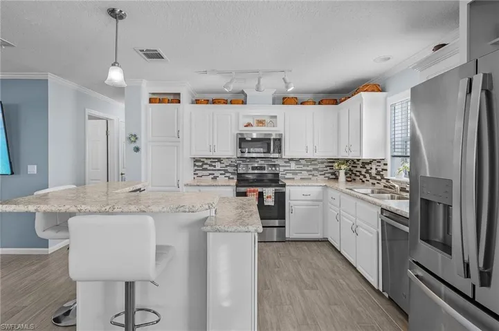 Kitchen featuring appliances with stainless steel finishes, hanging light fixtures, crown molding, a center island, and white cabinets