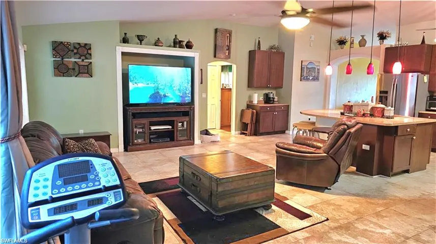 Living area with vaulted ceiling, a ceiling fan, arched walkways, and light tile patterned floors
