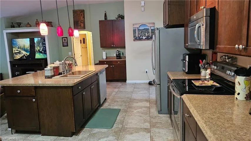 Kitchen with stainless steel appliances, a center island with sink, light countertops, pendant lighting, and dark brown cabinetry