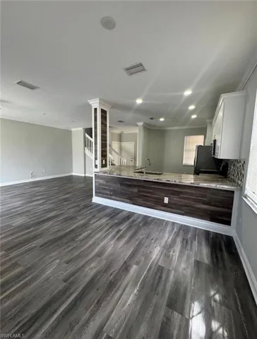 Kitchen with a peninsula, light stone countertops, dark wood-type flooring, crown molding, and open floor plan
