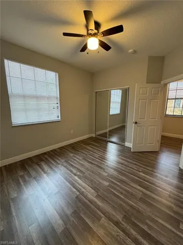 Unfurnished bedroom featuring dark wood-style floors, a textured ceiling, a closet, and a ceiling fan