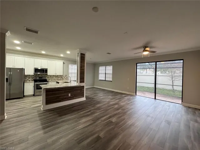 Kitchen featuring stainless steel appliances, open floor plan, white cabinetry, dark wood finished floors, and light stone counters