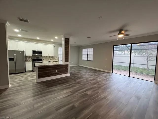 Kitchen with open floor plan, appliances with stainless steel finishes, white cabinets, crown molding, and dark wood-style floors