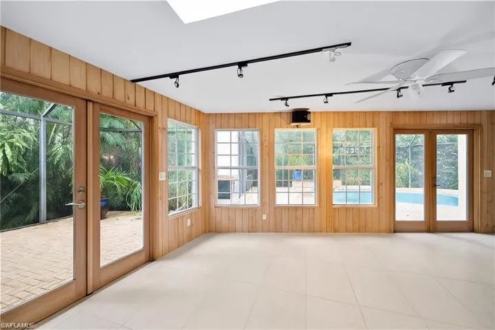 Unfurnished sunroom with french doors, wood walls, a skylight, and rail lighting