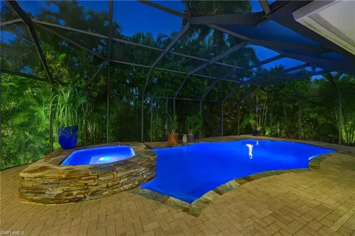 View of swimming pool featuring glass enclosure, a patio, and a pool with connected hot tub