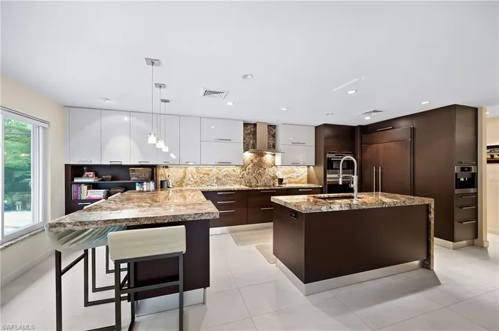 Kitchen with light tile patterned flooring, tasteful backsplash, paneled built in refrigerator, dark brown cabinetry, and a center island with sink