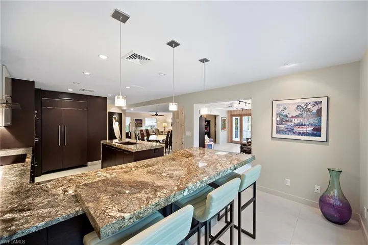 Kitchen with a breakfast bar, dark brown cabinets, light stone counters, a kitchen island, and ceiling fan