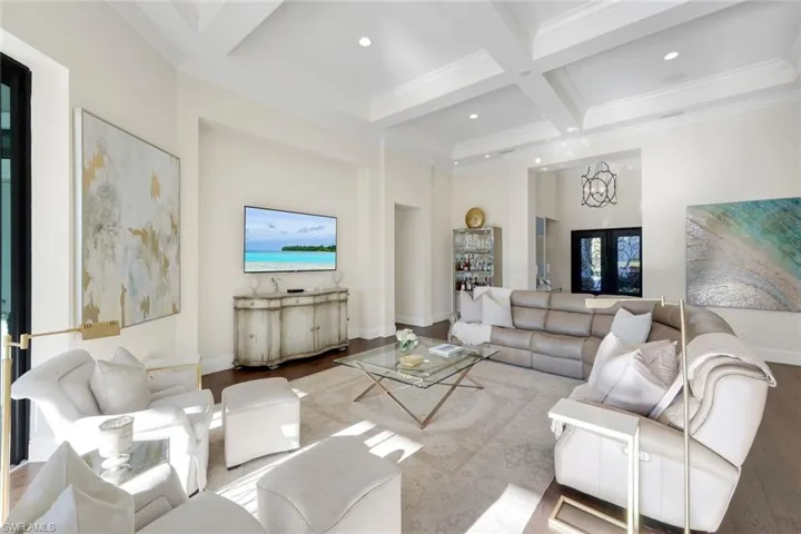 Living area with a towering ceiling, coffered ceiling, beam ceiling, wood finished floors, and crown molding throughout
