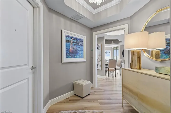 Hallway with ornamental molding, light hardwood / wood-style flooring, and a raised ceiling