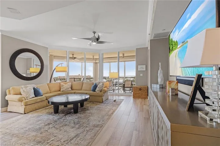 Living room featuring expansive windows, ceiling fan, light wood-type flooring, and crown molding