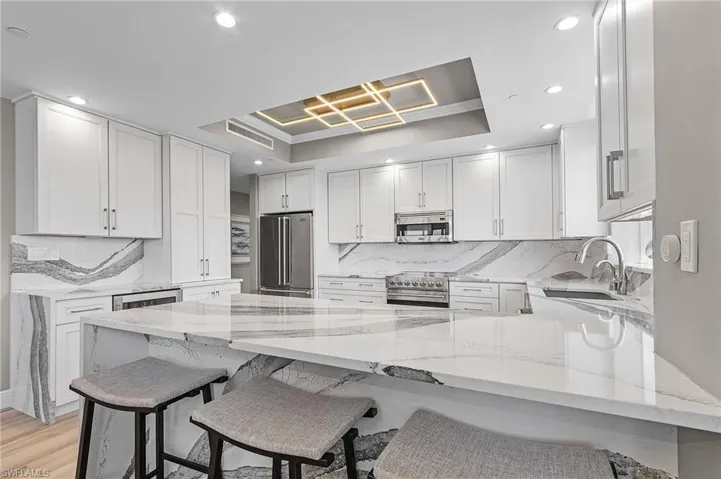 Kitchen with a breakfast bar area, light hardwood / wood-style flooring, stainless steel appliances, sink, and a tray ceiling