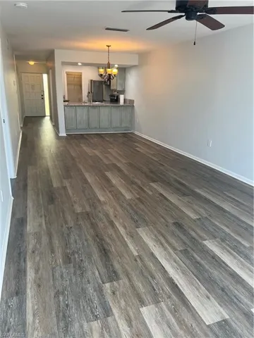 Unfurnished living room with hanging lights, dark wood-style flooring, and ceiling fan