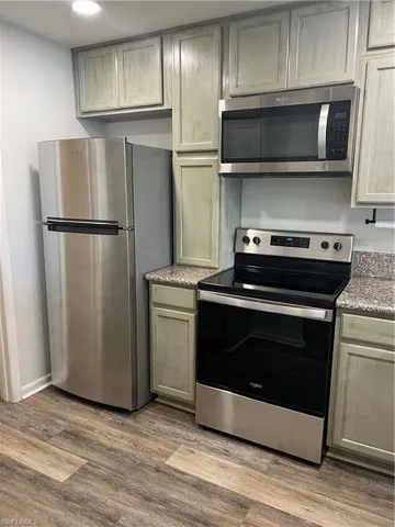 Kitchen featuring stainless steel appliances, dark wood-type flooring, and light stone counters