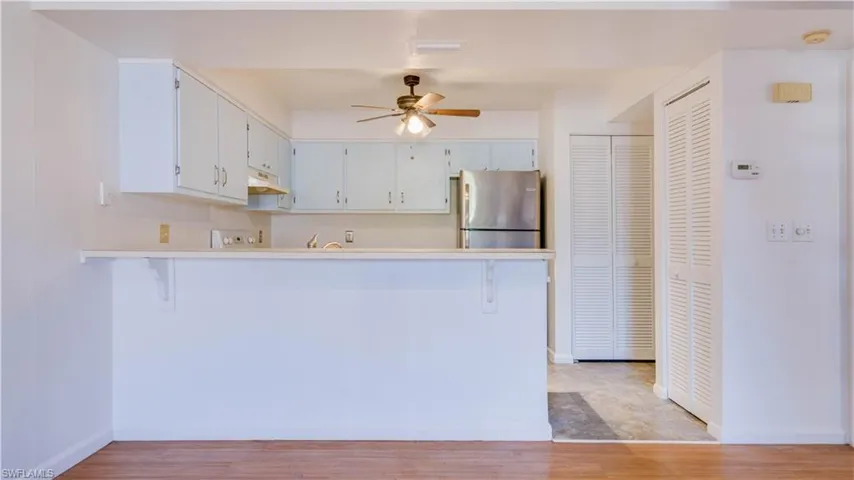 Kitchen featuring light countertops, a ceiling fan, freestanding refrigerator, a peninsula, and a breakfast bar area