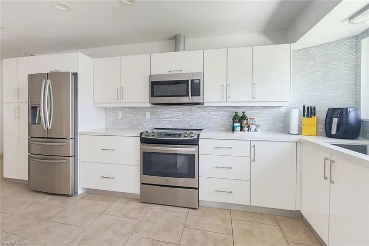 Kitchen featuring appliances with stainless steel finishes, light countertops, white cabinetry, light tile patterned floors, and backsplash