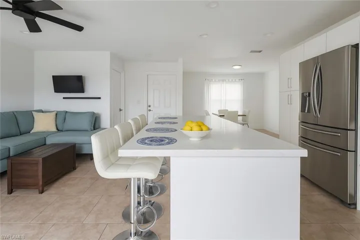 Kitchen with a breakfast bar, stainless steel fridge with ice dispenser, white cabinets, and light tile patterned flooring