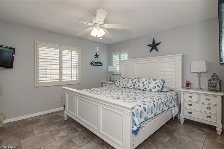 Spacious primary bedroom with tile flooring, plantation shutters, and coastal-inspired décor.