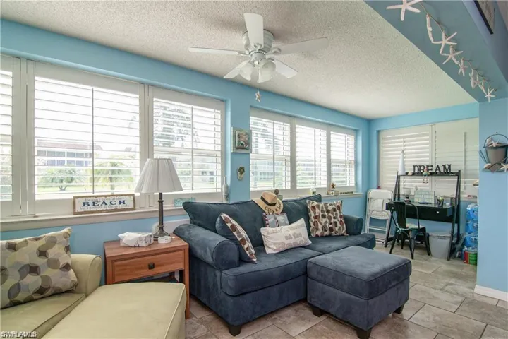 Bright sunroom featuring multiple windows with plantation shutters, a ceiling fan, and tile flooring