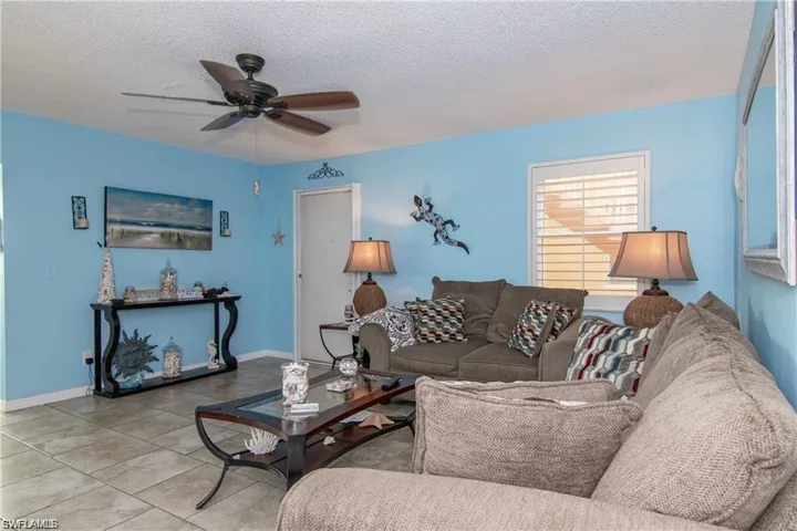 Spacious living area featuring tiled flooring, a ceiling fan, and window with plantation shutters