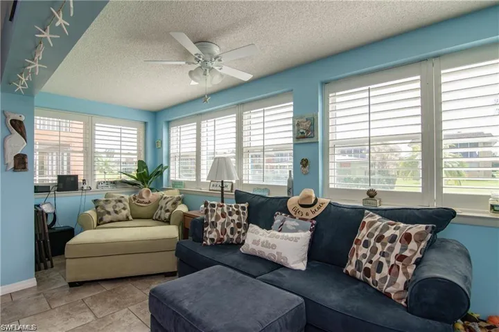 Light-filled room featuring multiple windows with white plantation shutters, a ceiling fan, and tile flooring
