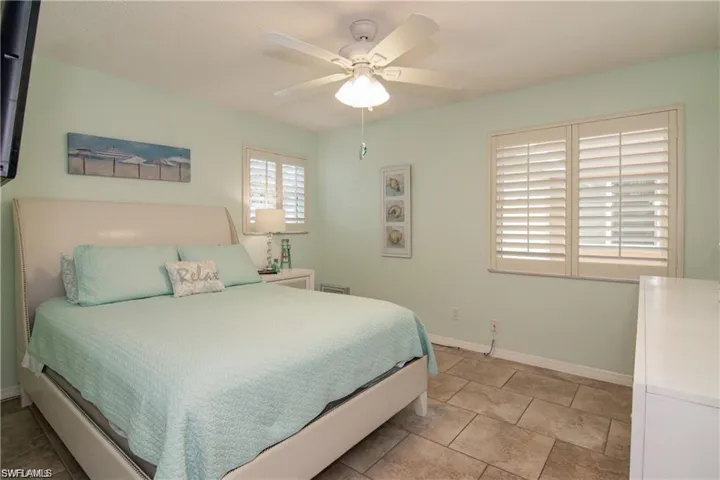 Spacious room featuring tile flooring, a ceiling fan, and two windows with plantation shutters
