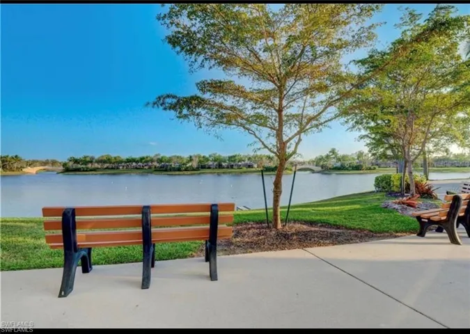 Waterfront scenery featuring a paved pathway, mature trees, and natural landscaping