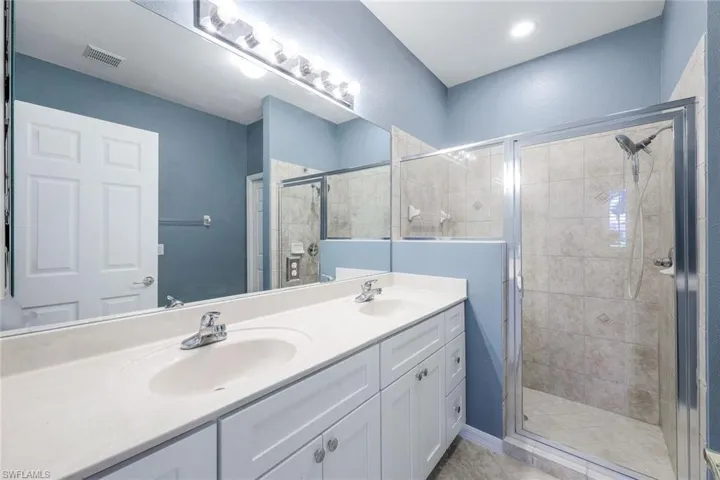 Bathroom with dual sinks, tile flooring, vanity with extensive cabinet space, and a shower with shower door