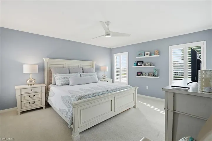 Master bedroom featuring multiple windows, plantation shutter window coverings, & modern fan
