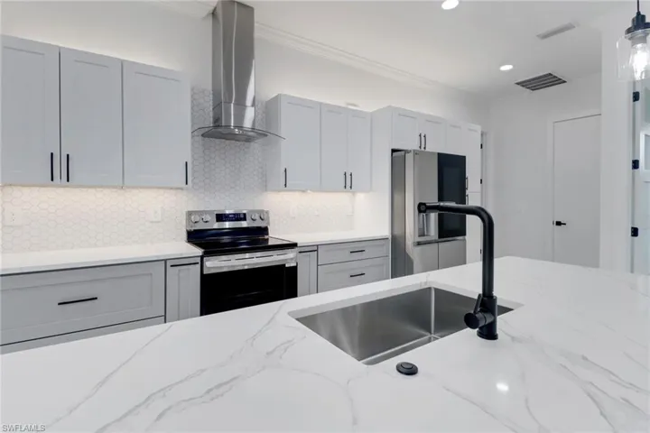 Kitchen featuring appliances with stainless steel finishes, wall chimney range hood, a sink, decorative backsplash, and hanging light fixtures