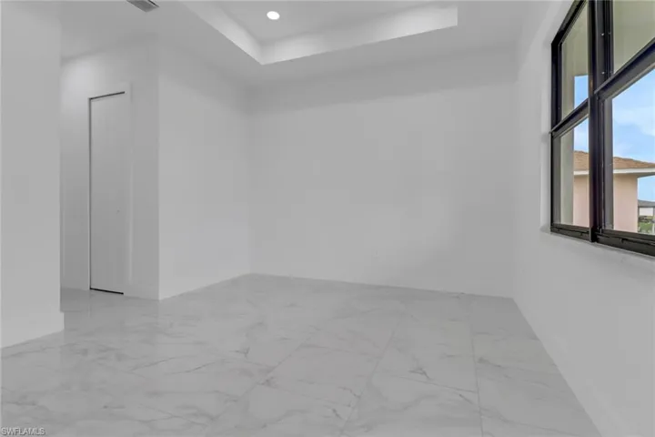 Spare room featuring baseboards, marble look tiles, a raised ceiling, and recessed lighting