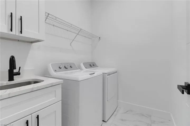 Washroom featuring independent washer and dryer, cabinet space, baseboards, and light marble finish floors