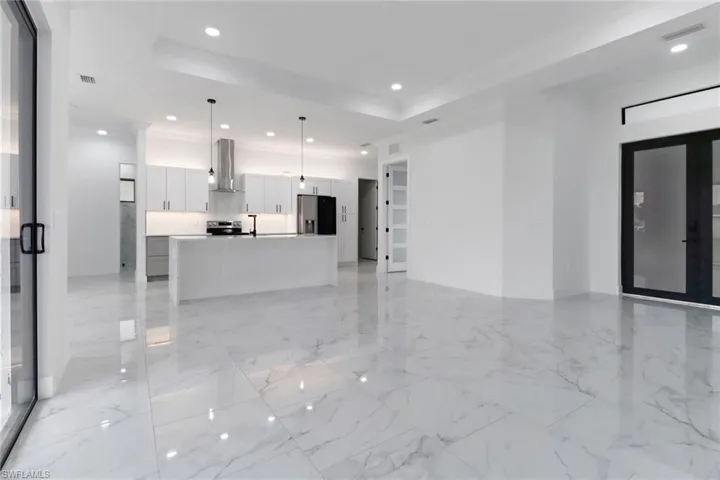 Unfurnished living room with recessed lighting, a tray ceiling, crown molding, and light marble finish floors