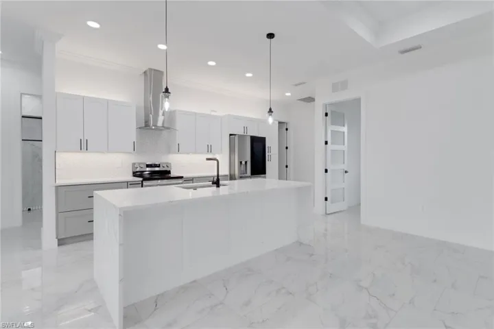 Kitchen with appliances with stainless steel finishes, wall chimney exhaust hood, crown molding, a sink, and an island with sink