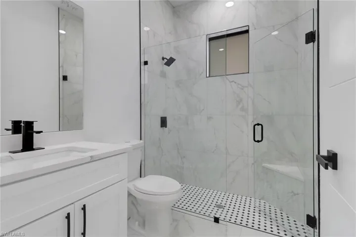 Bathroom featuring marble finish floors, a marble finish shower, toilet, and vanity