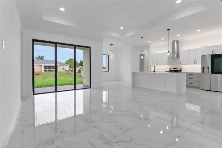Unfurnished living room featuring a raised ceiling, a sink, recessed lighting, and light marble finish floors
