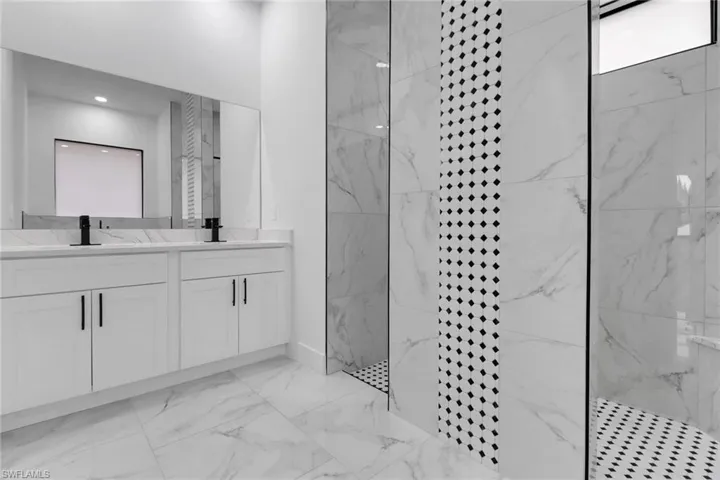 Bathroom with a marble finish shower, marble finish flooring, double vanity, and baseboards